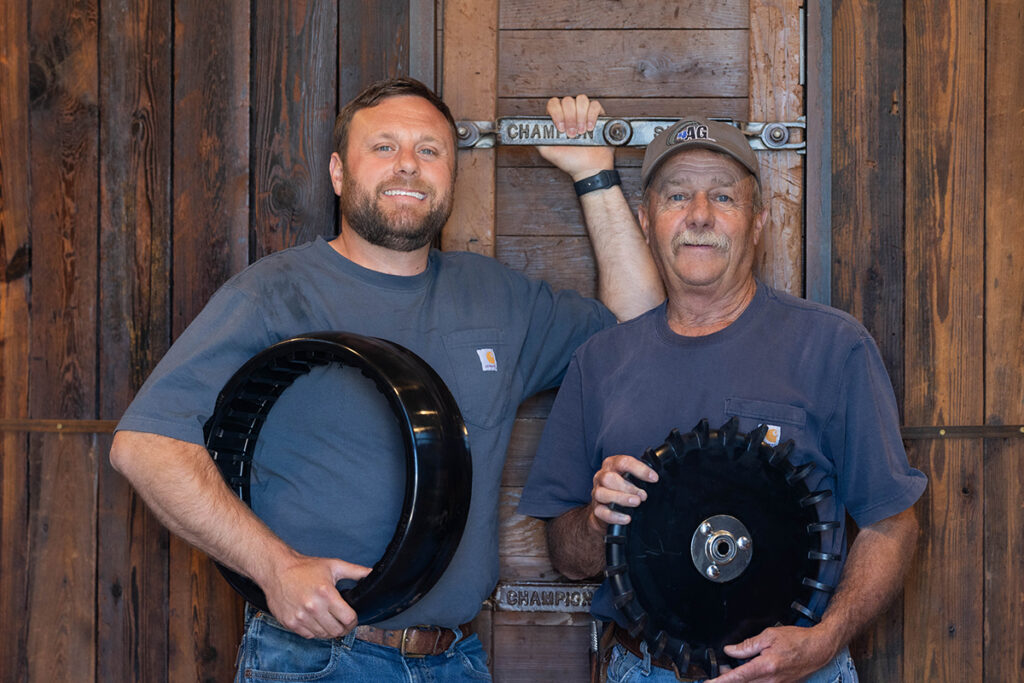Two men holding 4AG gauge wheel and closing wheel in front of a wood wall