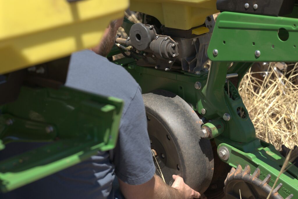 Farmer looking at planter gauge wheels mounted on a tractor, checking depth control and wheel condition for accurate seed placement.