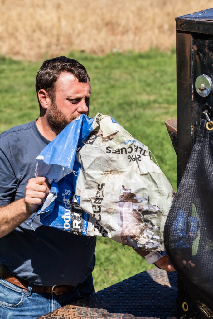 A rancher places a feed sack into the Catch-All mounted on flatbed equipment, demonstrating its practical cleanup benefits.
