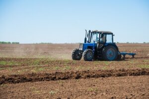 Blue tractor operating in a dry field before no till planting with no till equipment