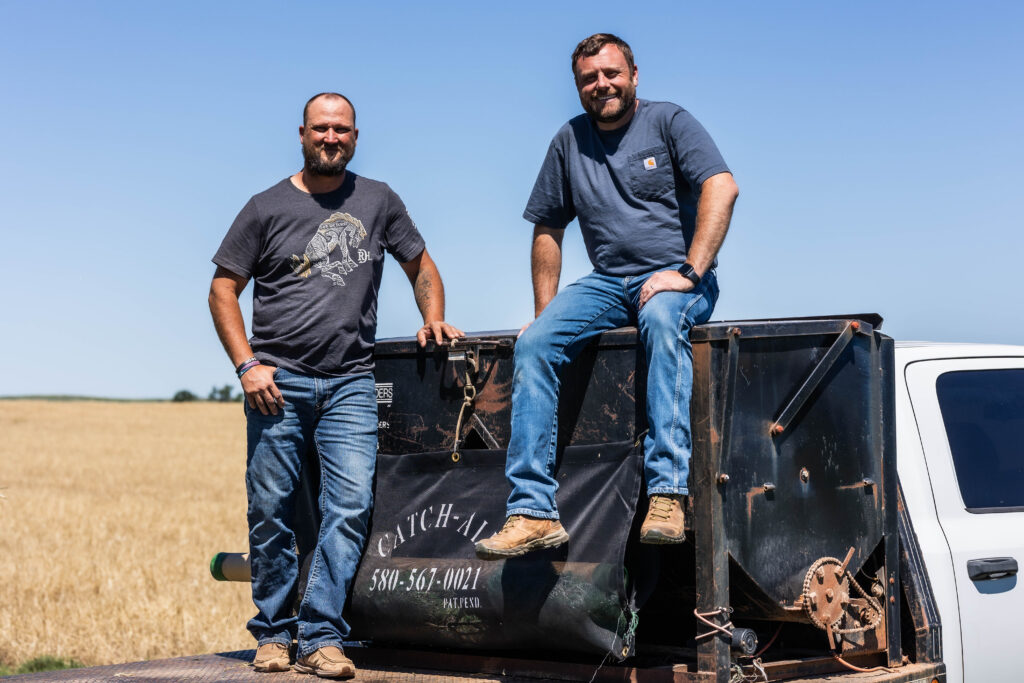 Ranchers standing on flatbed equipment with Catch All installed to control hay bale netting on working flatbeds carrying farming supplies.