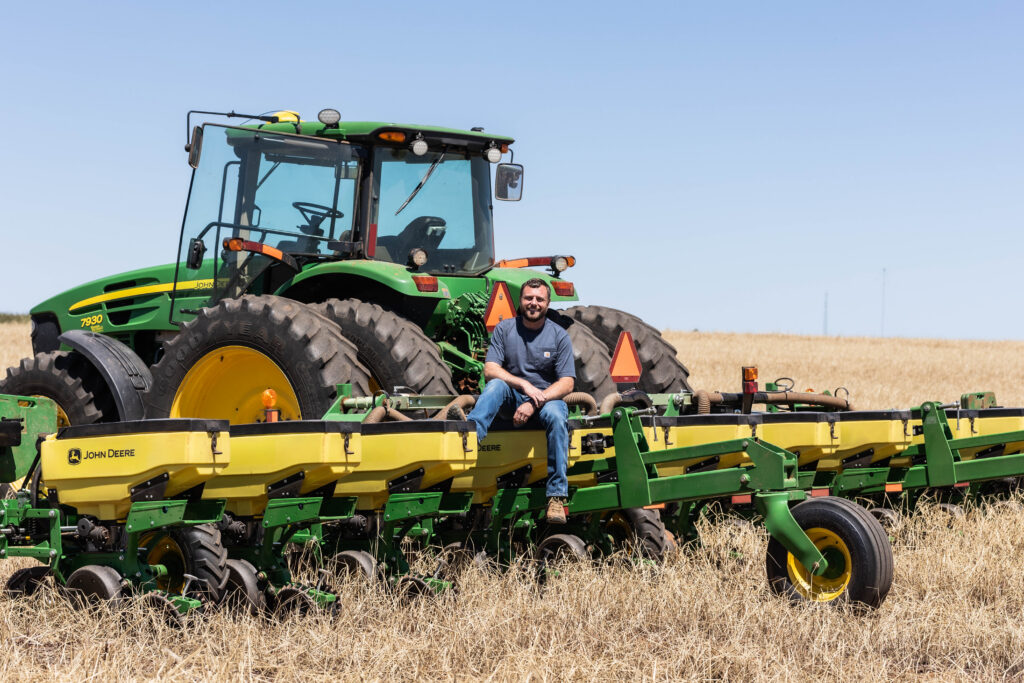 Farmer sitting on a John Deere planter in a no-till farming field with cultivator gauge wheels and precision agriculture equipment designed for soil cultivation.