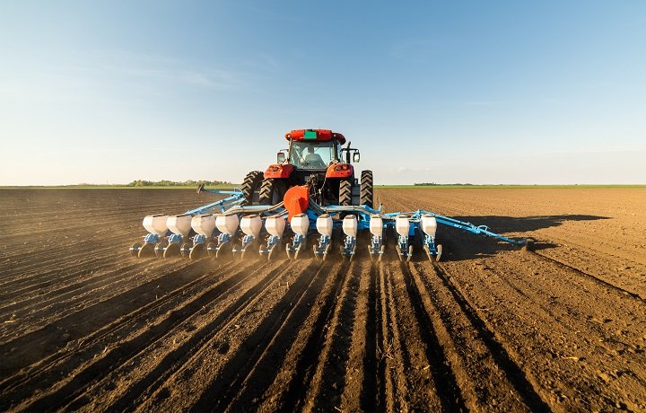 Tractor using cultivator gauge wheels during tillage farming and soil cultivation in a large agricultural field with modern no-till farming equipment.