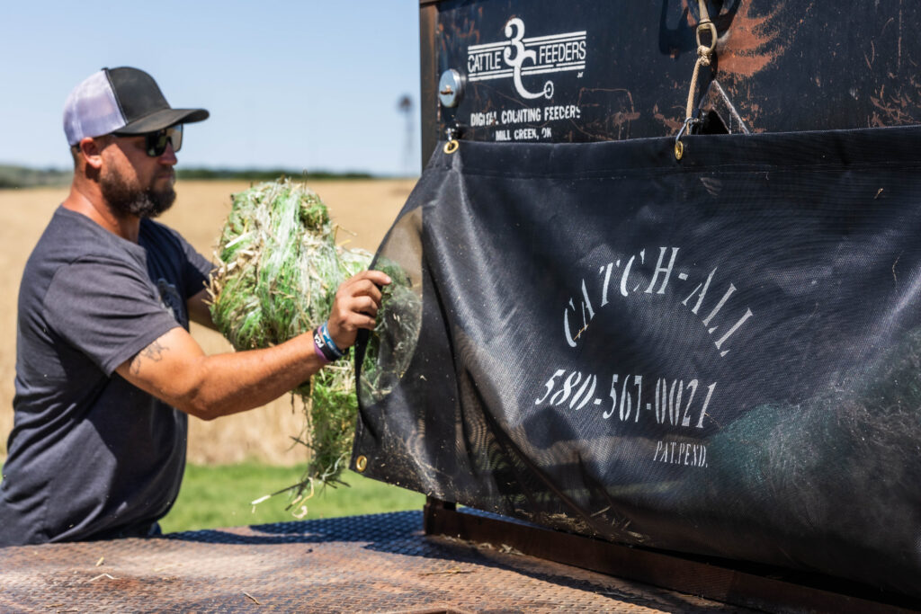 Rancher placing hay bale netting into the Catch-All net sack mounted on a feed truck, demonstrating practical ranch clean up tools for everyday feeding operations.