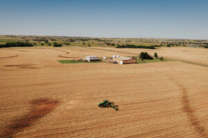 Aerial view of Oklahoma agriculture with a tractor working across harvested fields, showcasing the dedication of an Oklahoma farmer and modern farming practices.