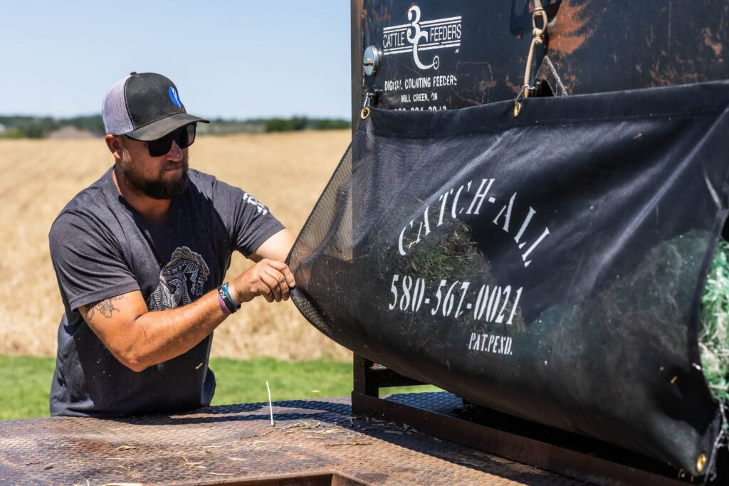Rancher using a net sack to contain hay bale netting on flatbeds, keeping farming supplies organized and loose wrap away from a cube feeder.