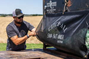Rancher using a net sack to contain hay bale netting on flatbeds, keeping farming supplies organized and loose wrap away from a cube feeder.